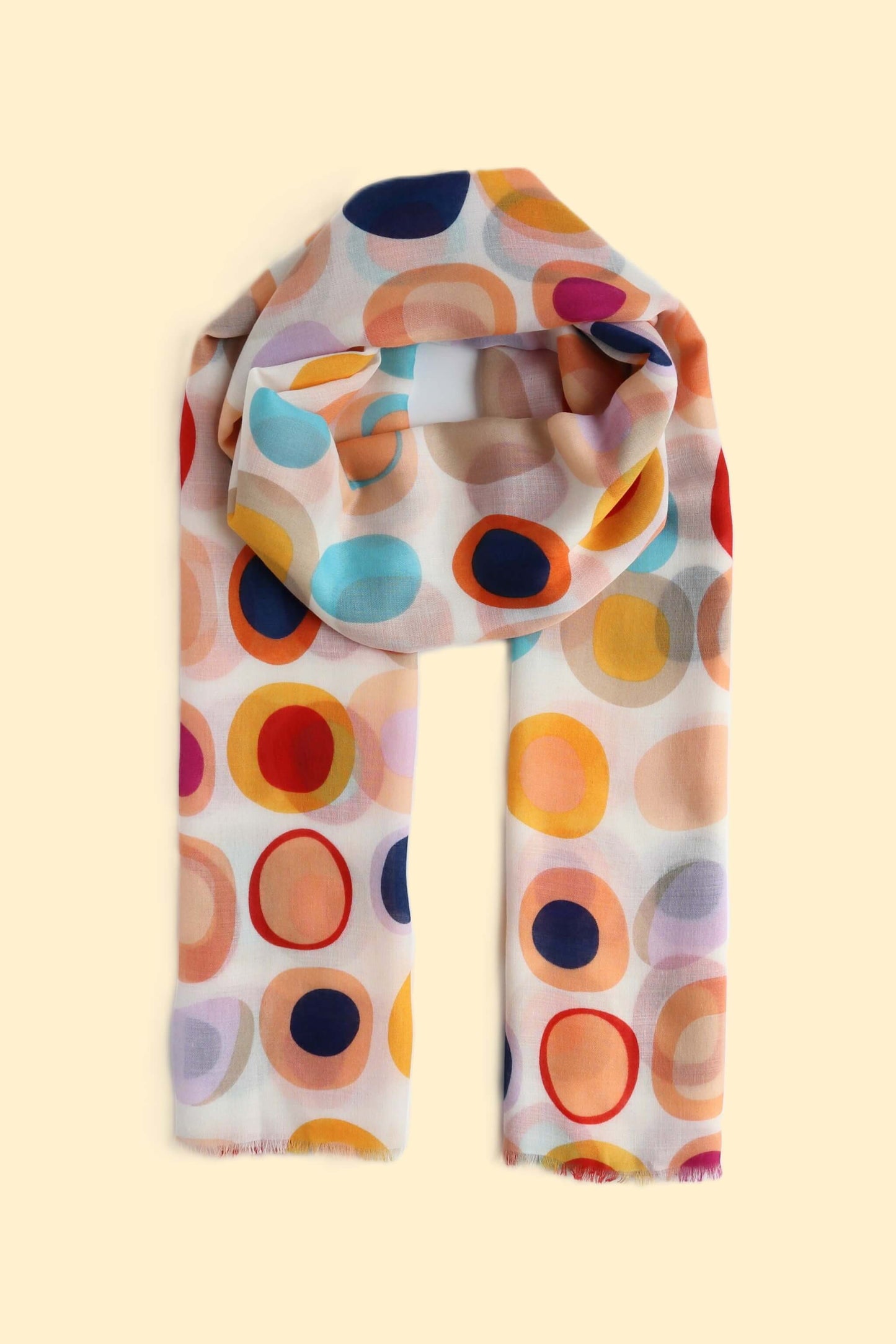 Creamy white scarf with a bold retro circle and oval pattern in navy, orange, yellow, red, pink, and blue. Lightweight fabric with a soft fringe.