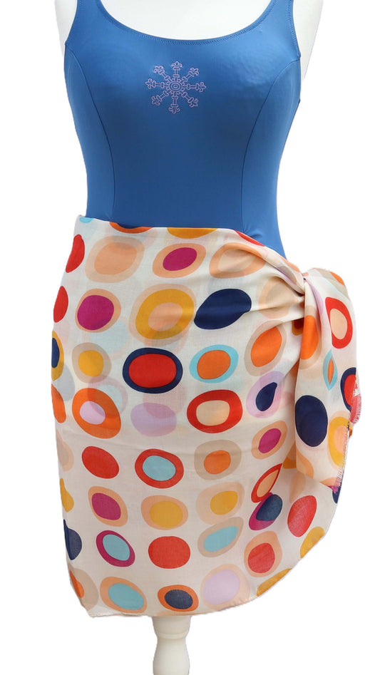 Creamy white beach wrap featuring a bold, mod-inspired oval and dot design in navy, orange, pink, and light blue. Light, airy fabric tied at the waist.