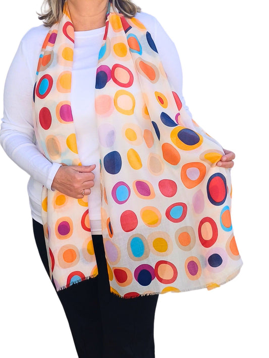 Creamy white scarf with a bold retro circle and oval design in navy, red, orange, yellow, pink, and blue. Soft, lightweight fabric with fringed edges.