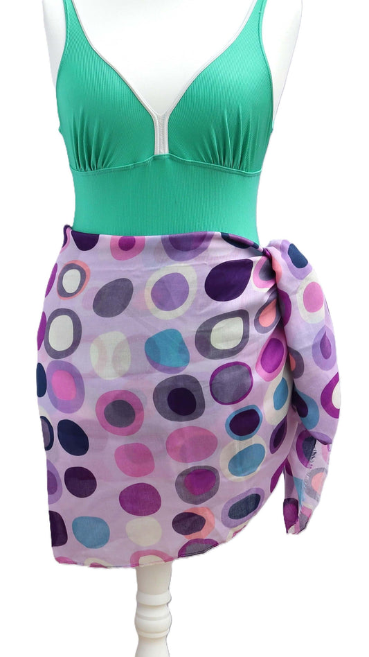 Lilac beach sarong with a vibrant, retro-inspired dot pattern in purple, pink, blue, and white. Lightweight, semi-sheer fabric tied at the hip.