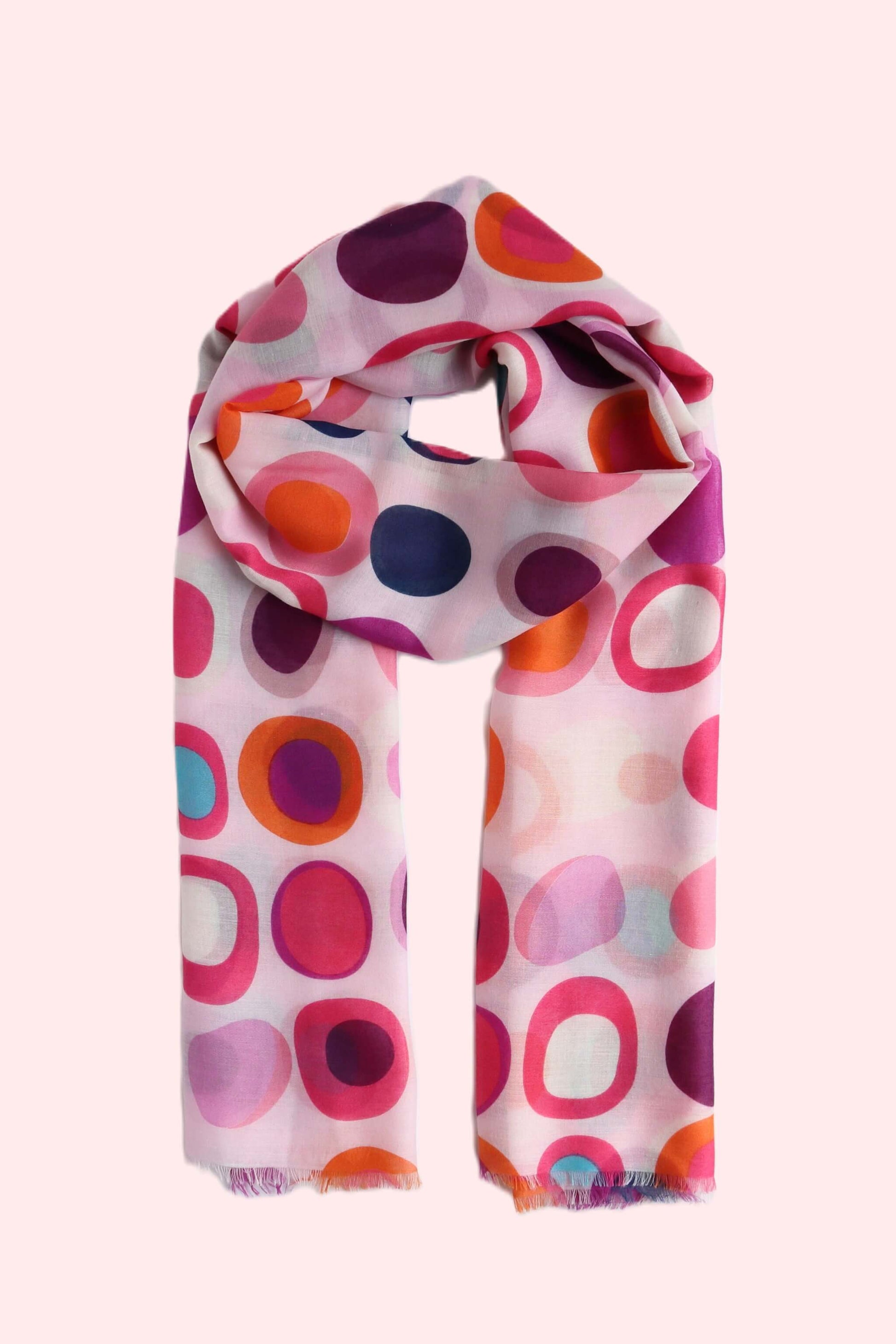 Pale pink scarf with a vibrant retro circle and oval design in fuchsia, orange, purple, and blue. Lightweight fabric with a soft drape and subtle fringe.