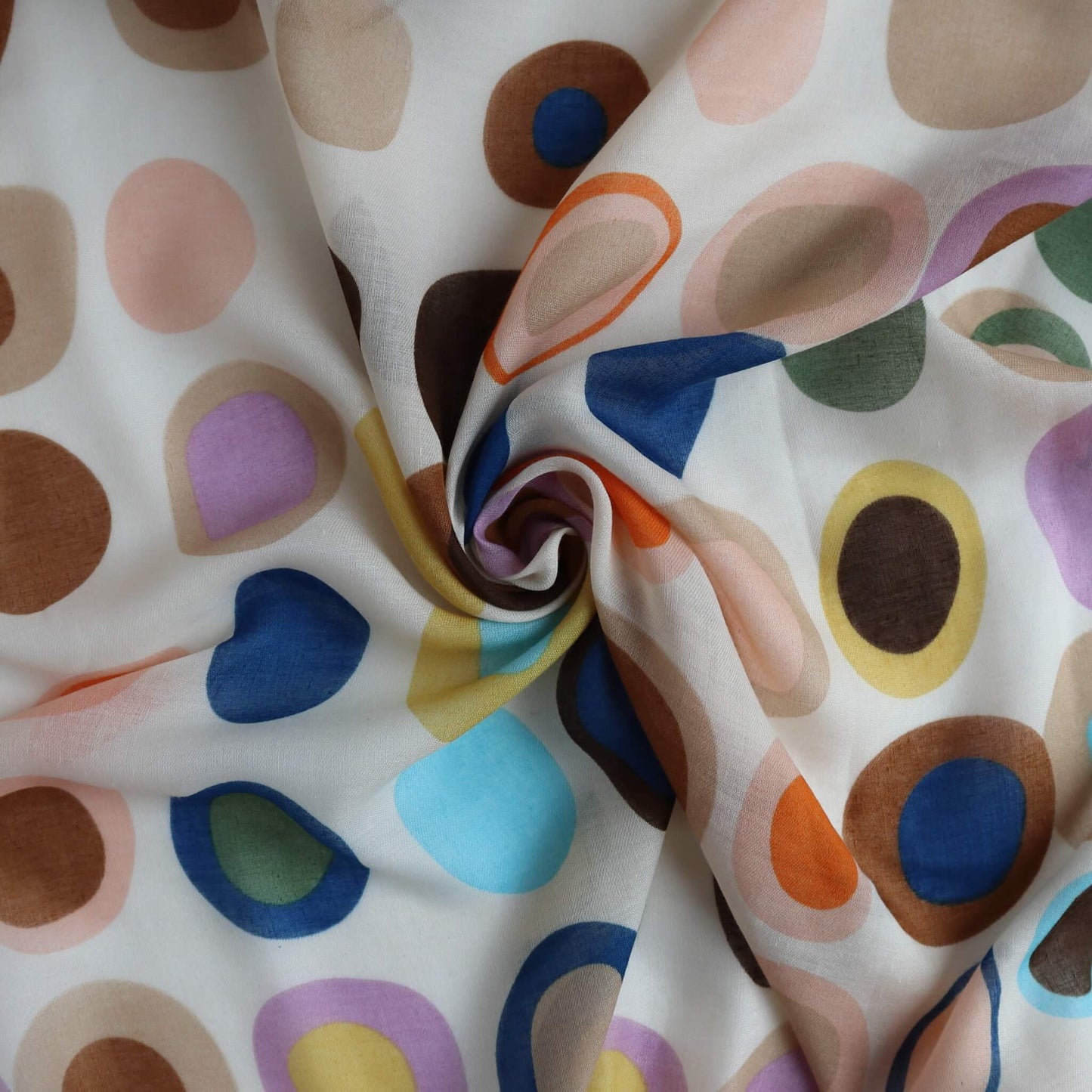 Beige scarf fabric with a playful circle and oval design in brown, blue, pink, lilac, and yellow. Light, flowing textile with a central swirl.