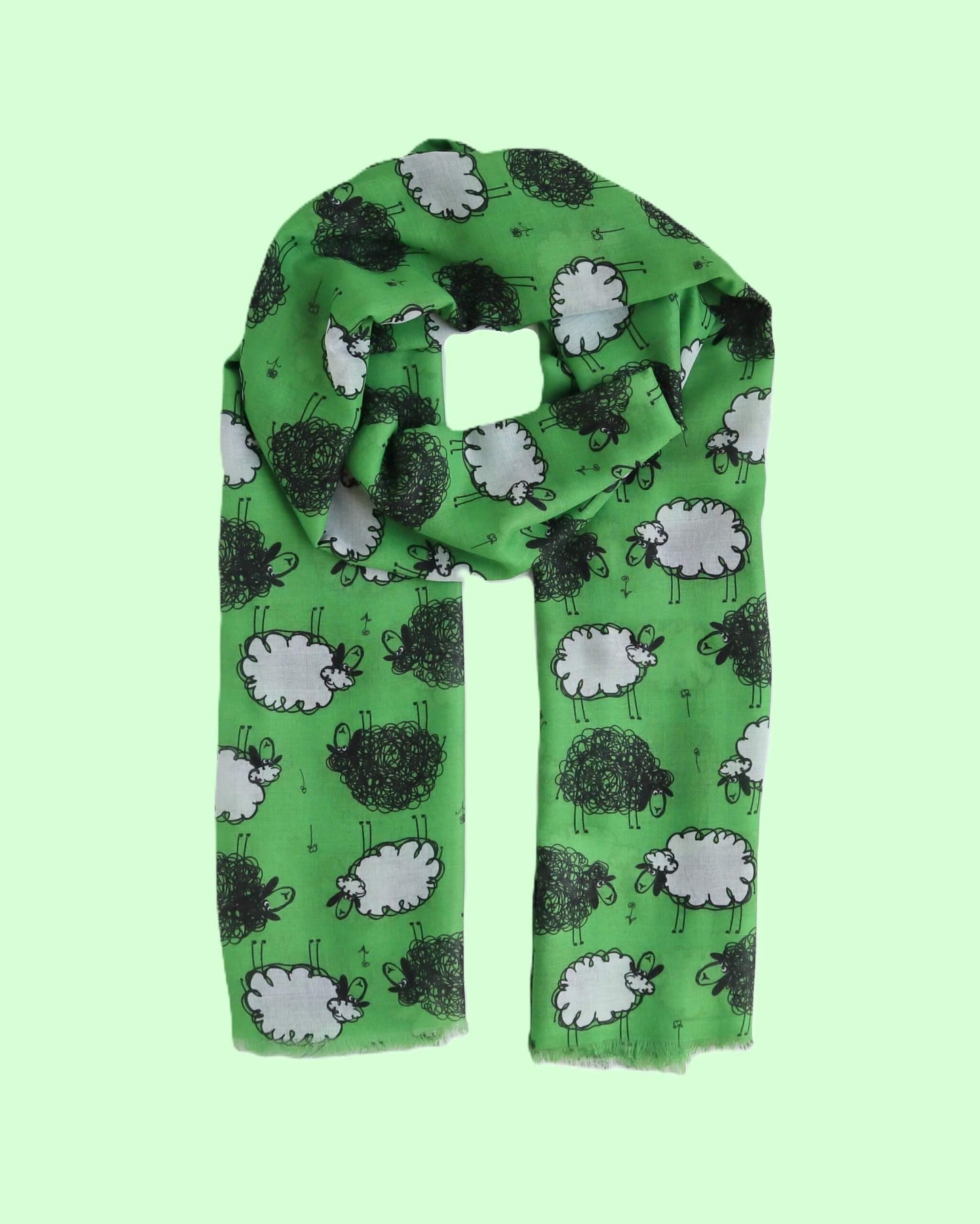 Bright green scarf with a playful design of black and white sheep figures. Lightweight fabric with a soft, draped appearance and fringed edges.