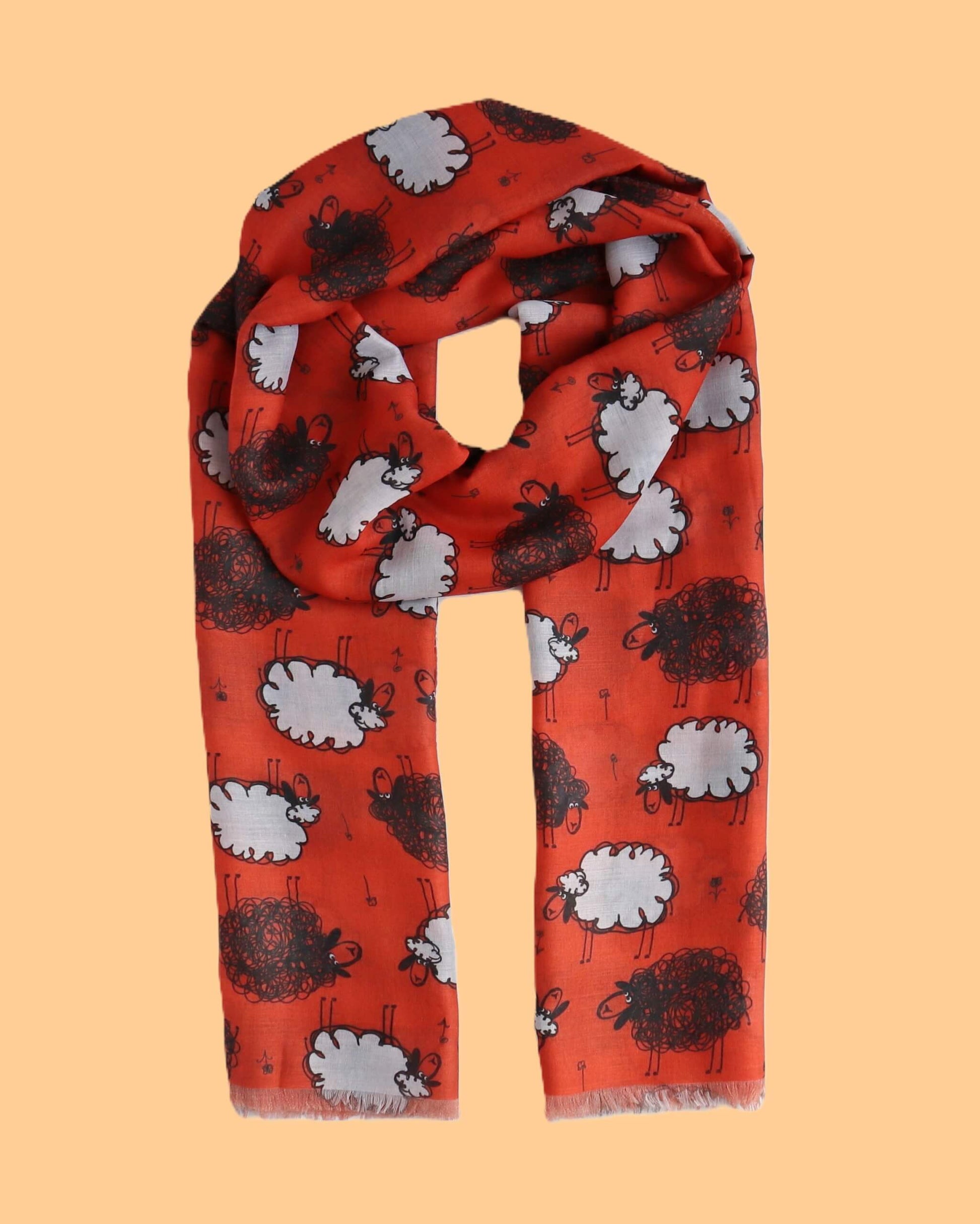 Vivid red scarf featuring a fun pattern of black and white sheep illustrations. Soft, flowing material with a delicate fringe along the edges.