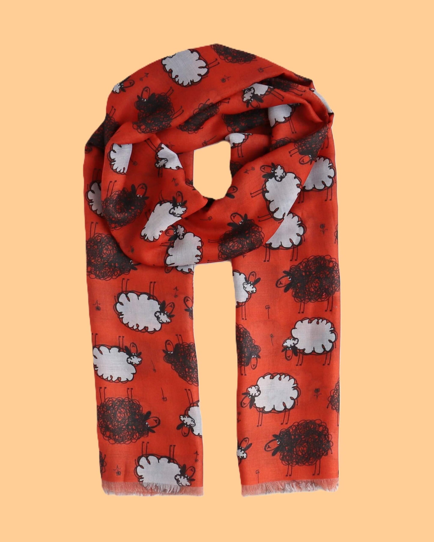Vivid red scarf featuring a fun pattern of black and white sheep illustrations. Soft, flowing material with a delicate fringe along the edges.
