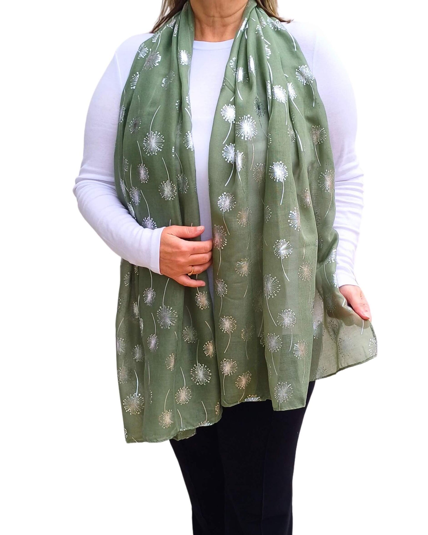 A person wearing a green scarf with a metallic silver foiled dandelion print, paired with a white top and black pants.