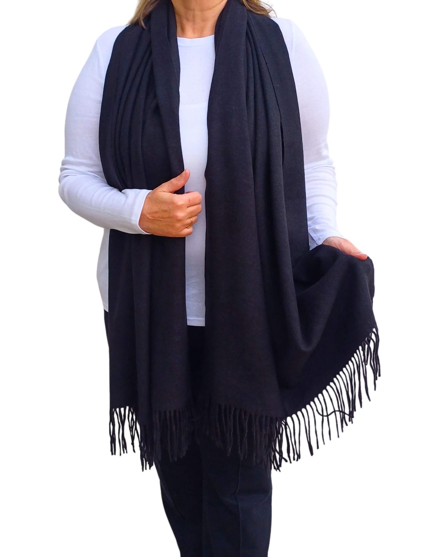 Aurora's Array: Woman models a soft, warm black wool blend scarf with fringed edges, draped around her neck and shoulders.