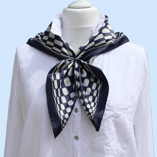 Aurora's Array: The Chic Satin Square Scarf - A navy blue and white patterned satin scarf tied neatly around the neck of a mannequin wearing a white collared shirt.
