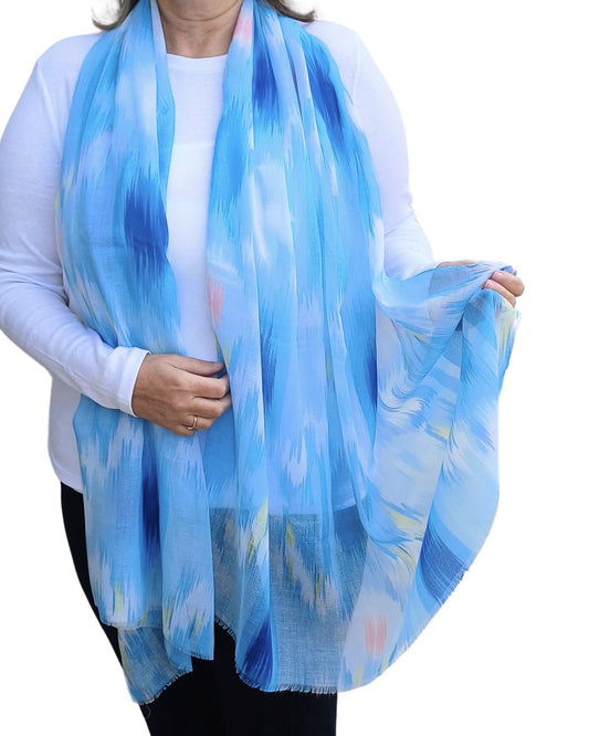 Lightweight blue scarf with an abstract ikat-inspired print in shades of blue, white, yellow, and pink. Soft, flowing fabric.