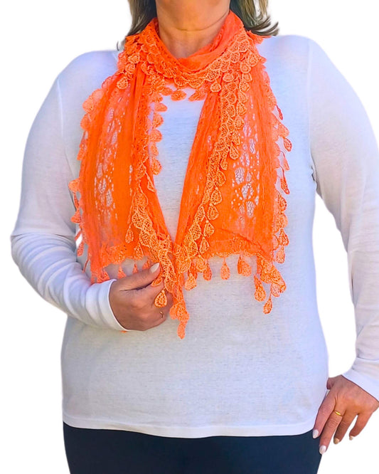 Aurora's Array: Woman models a vibrant orange lace scarf with a delicate leaf-like pattern and fringed edges.
