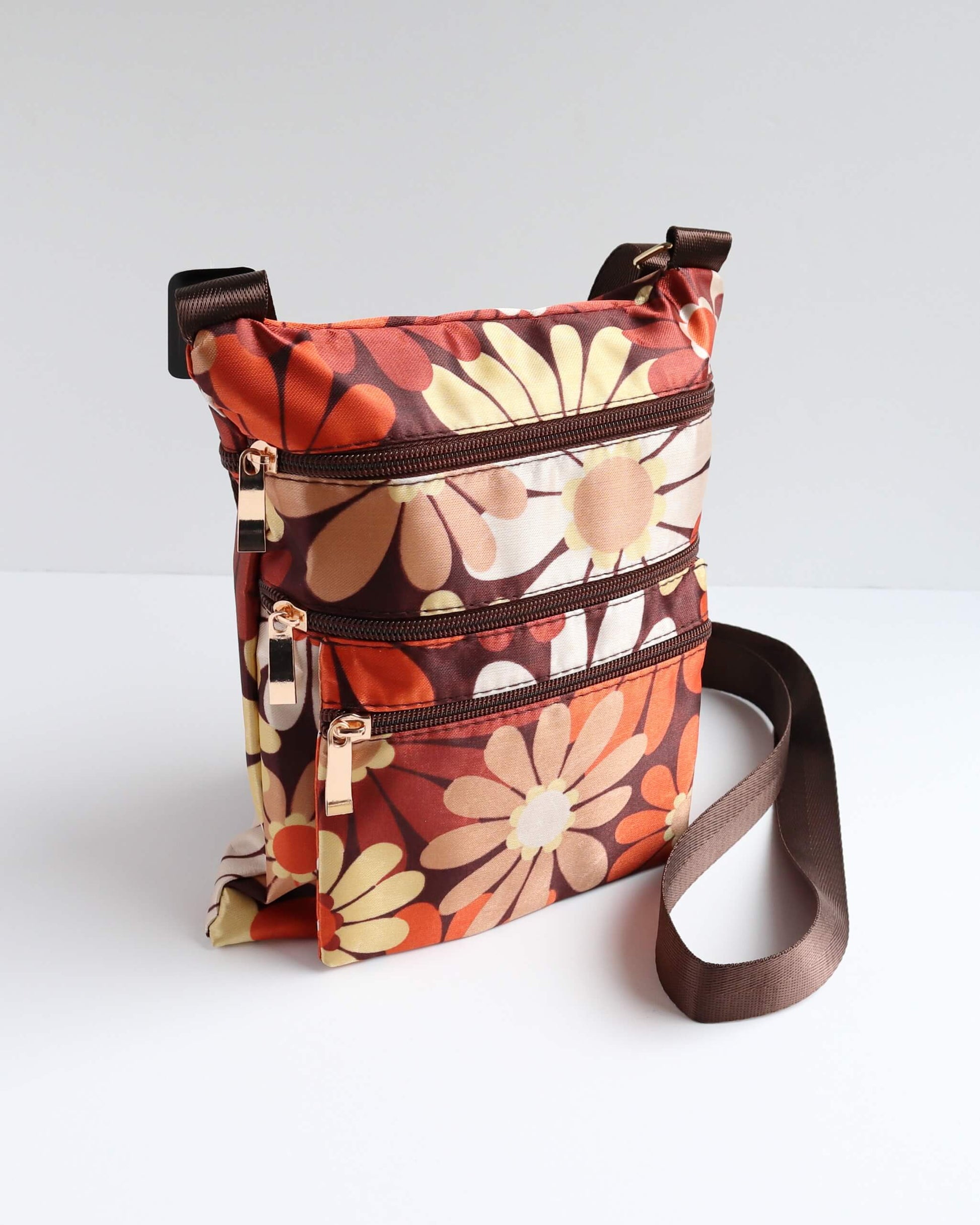 Retro floral crossbody bag in shades of brown, orange, and cream with a brown strap and trim. Features three zippered sections.