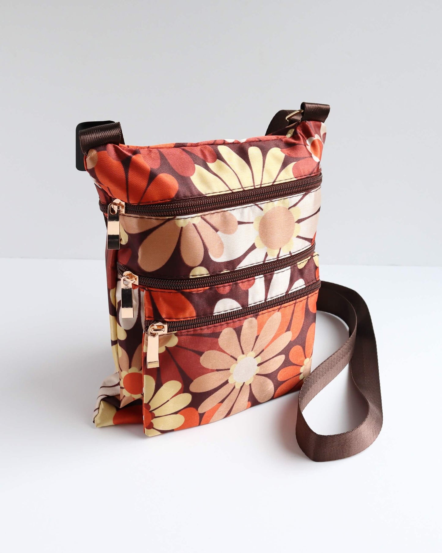 Retro floral crossbody bag in shades of brown, orange, and cream with a brown strap and trim. Features three zippered sections.