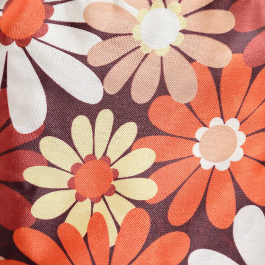 Close-up of a crossbody bag's fabric: a retro daisy chain print in shades of brown, orange, cream, and yellow. Detailed floral pattern.