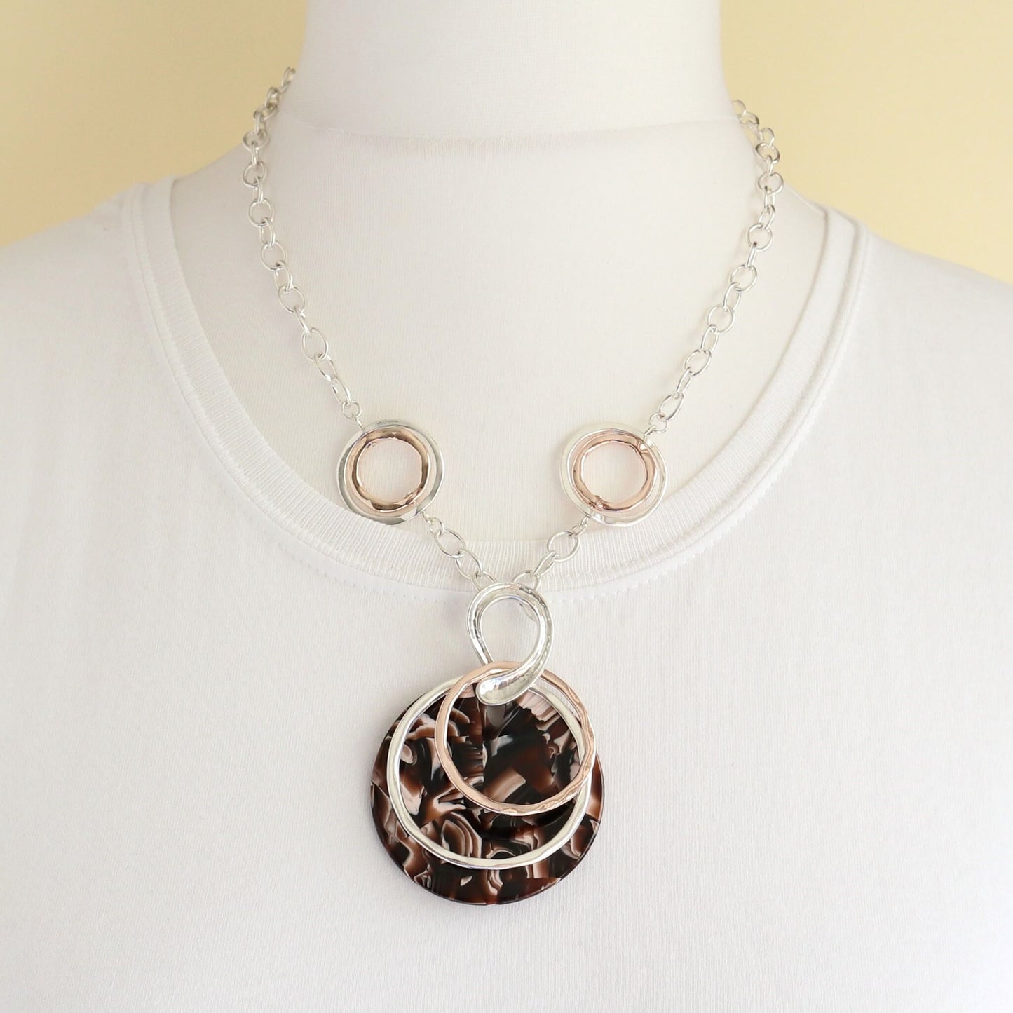 Silver chain necklace with interlocking silver and rose gold tone rings, and a large brown marble effect disc pendant.