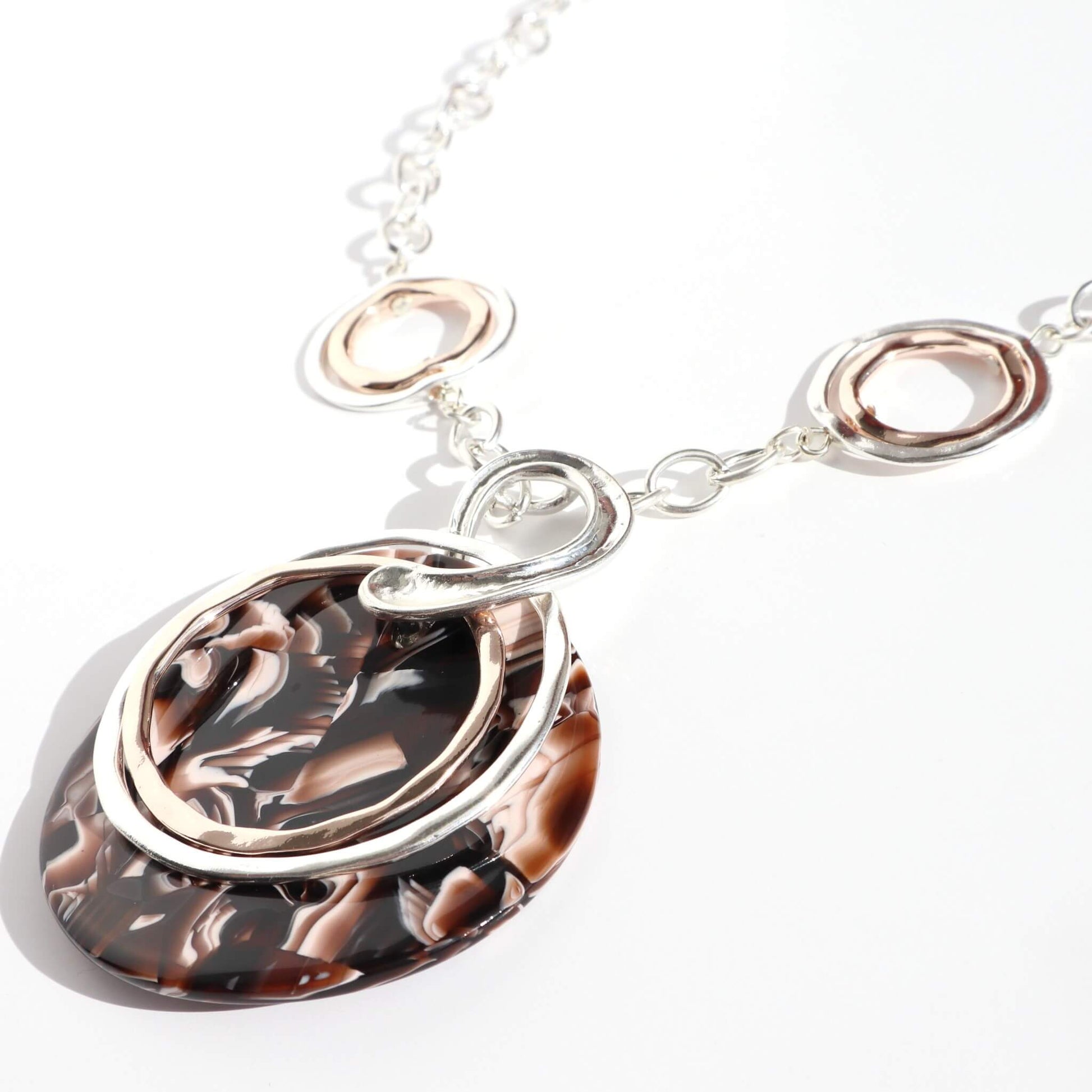Silver tone chain necklace with interlocking silver and rose gold tone rings, featuring a large brown marble effect oval pendant.