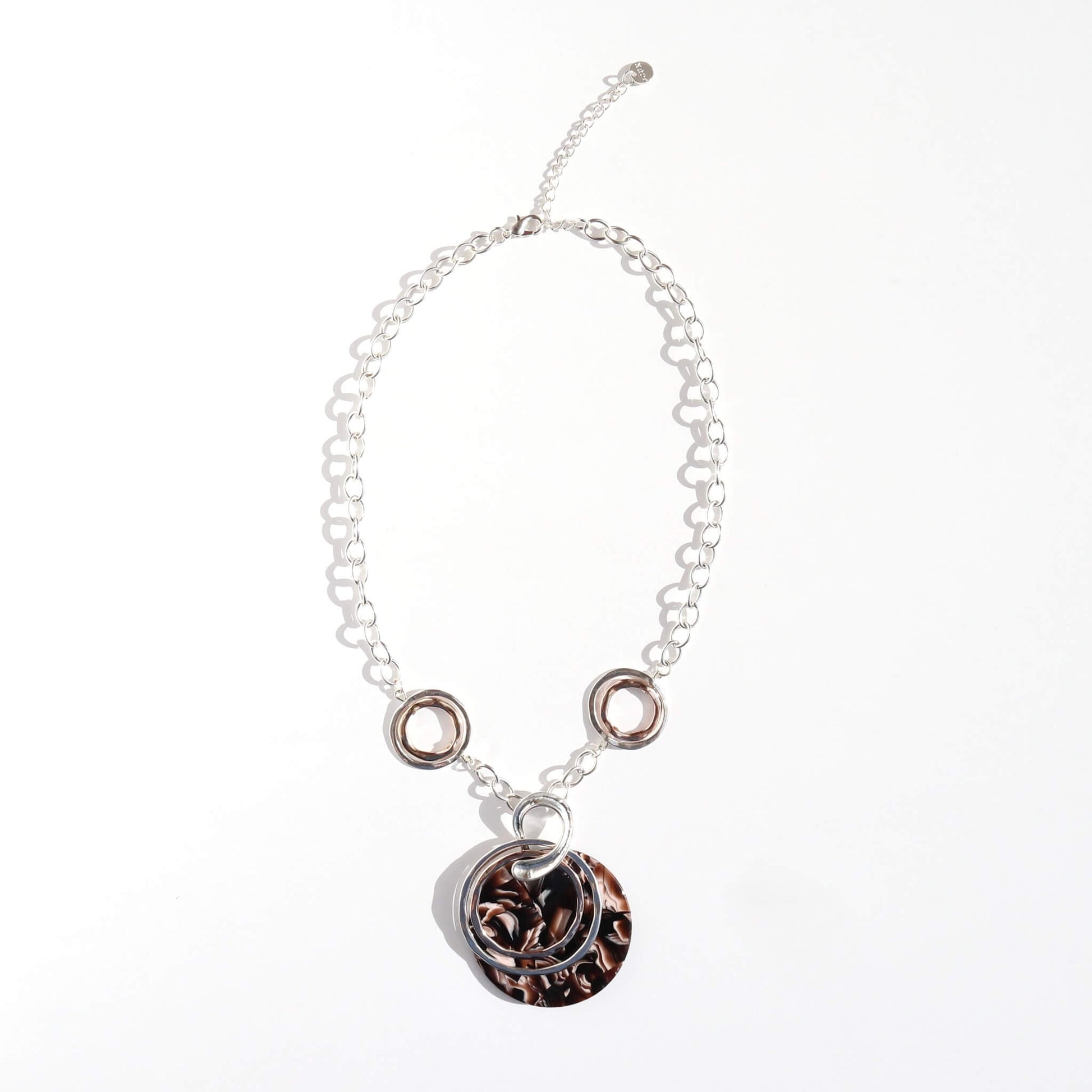 Silver tone chain necklace with silver and rose gold tone rings, featuring a large round pendant with a brown marble effect pattern. Adjustable length.