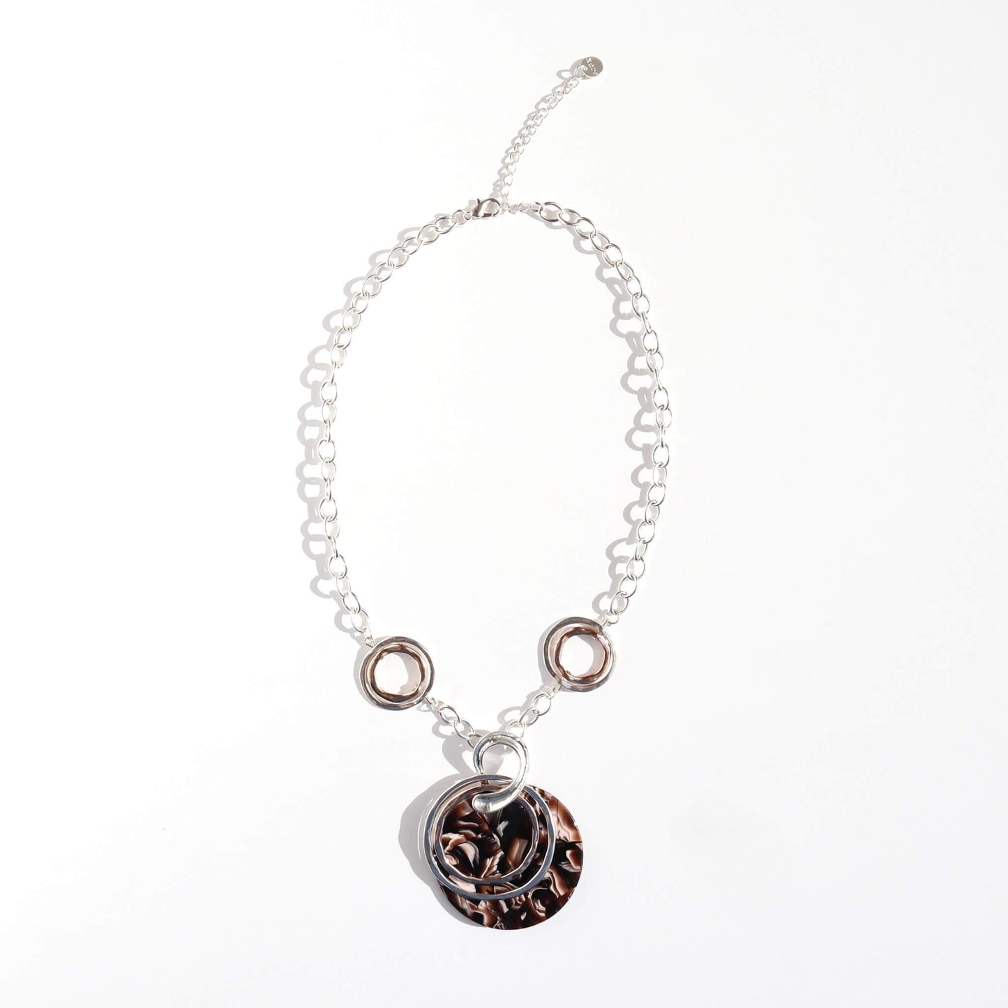 Silver tone chain necklace with silver and rose gold tone rings, featuring a large round pendant with a brown marble effect pattern. Adjustable length.