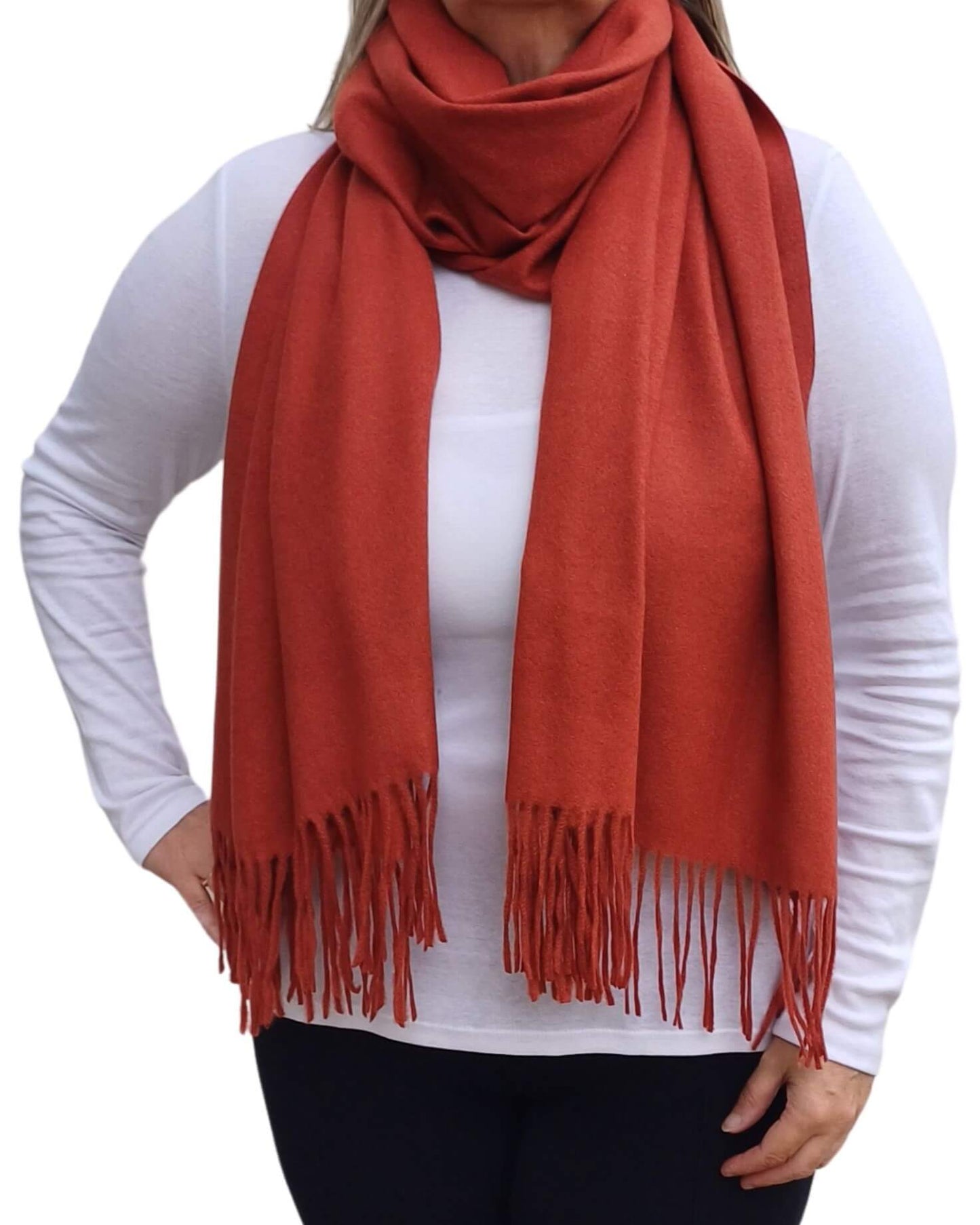 Aurora's Array: Woman models a soft, warm burnt orange wool blend scarf with fringed edges, draped around her neck and shoulders.