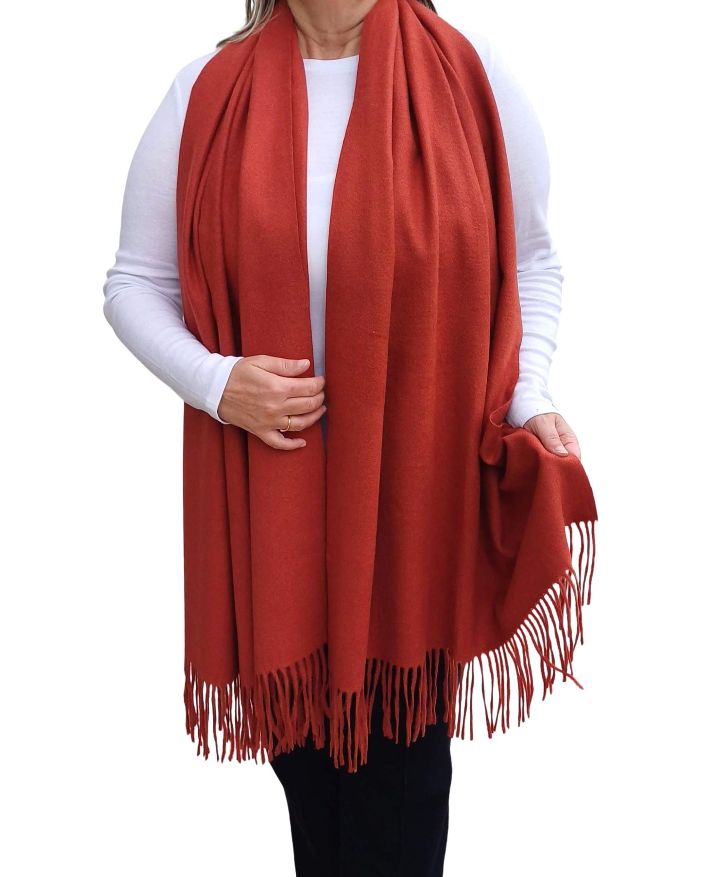 Aurora's Array: Woman models a soft, warm terracotta, rust orange wool blend scarf with fringed edges, draped around her neck and shoulders.
