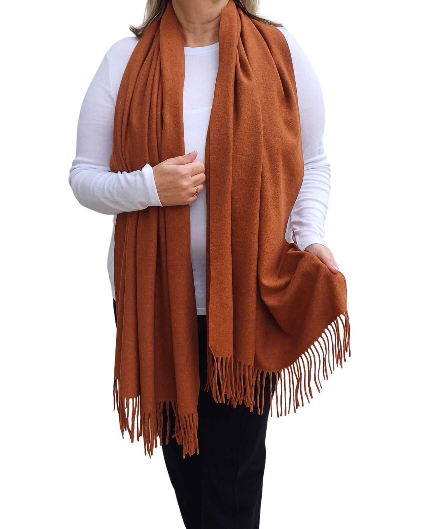 Aurora's Array: Woman models a soft, warm caramel, camel brown wool blend scarf with fringed edges, draped around her neck and shoulders.