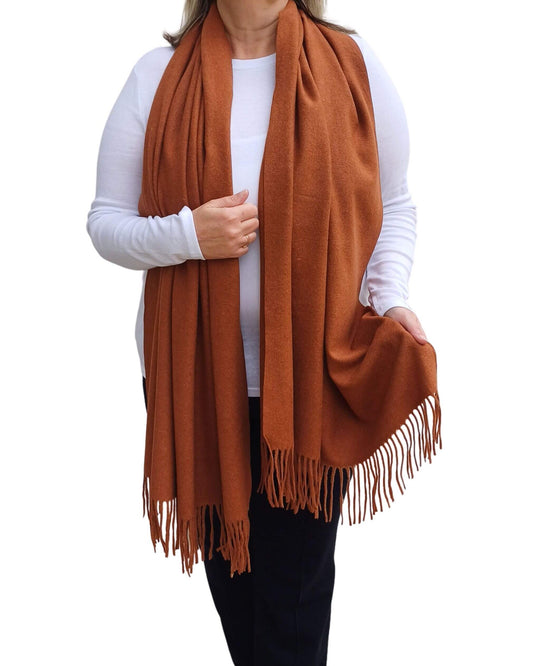Aurora's Array: Woman models a soft, warm caramel, camel brown wool blend scarf with fringed edges, draped around her neck and shoulders.
