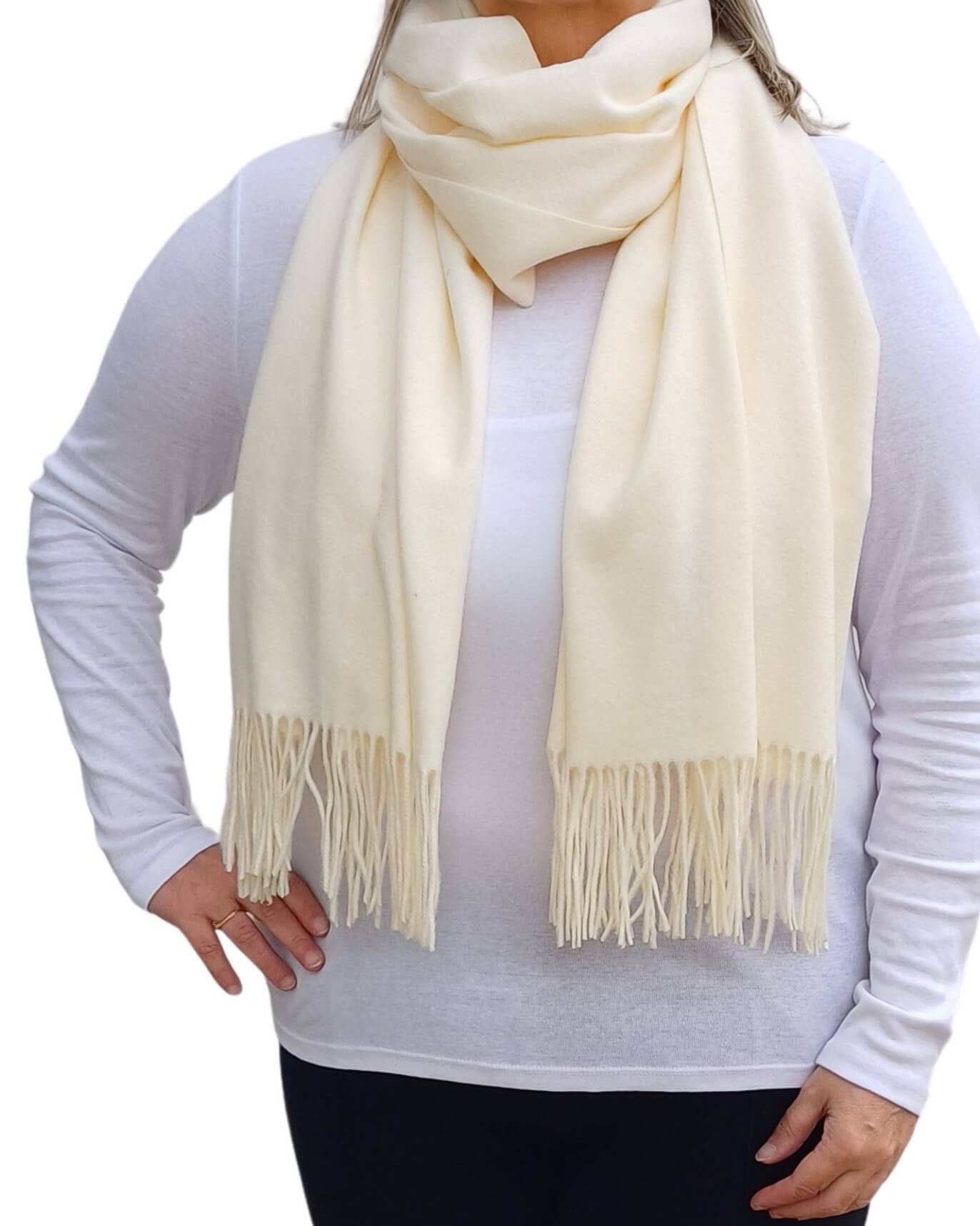 Aurora's Array: Woman models a soft, warm off-white cream wool blend scarf with fringed edges, draped around her neck and shoulders.