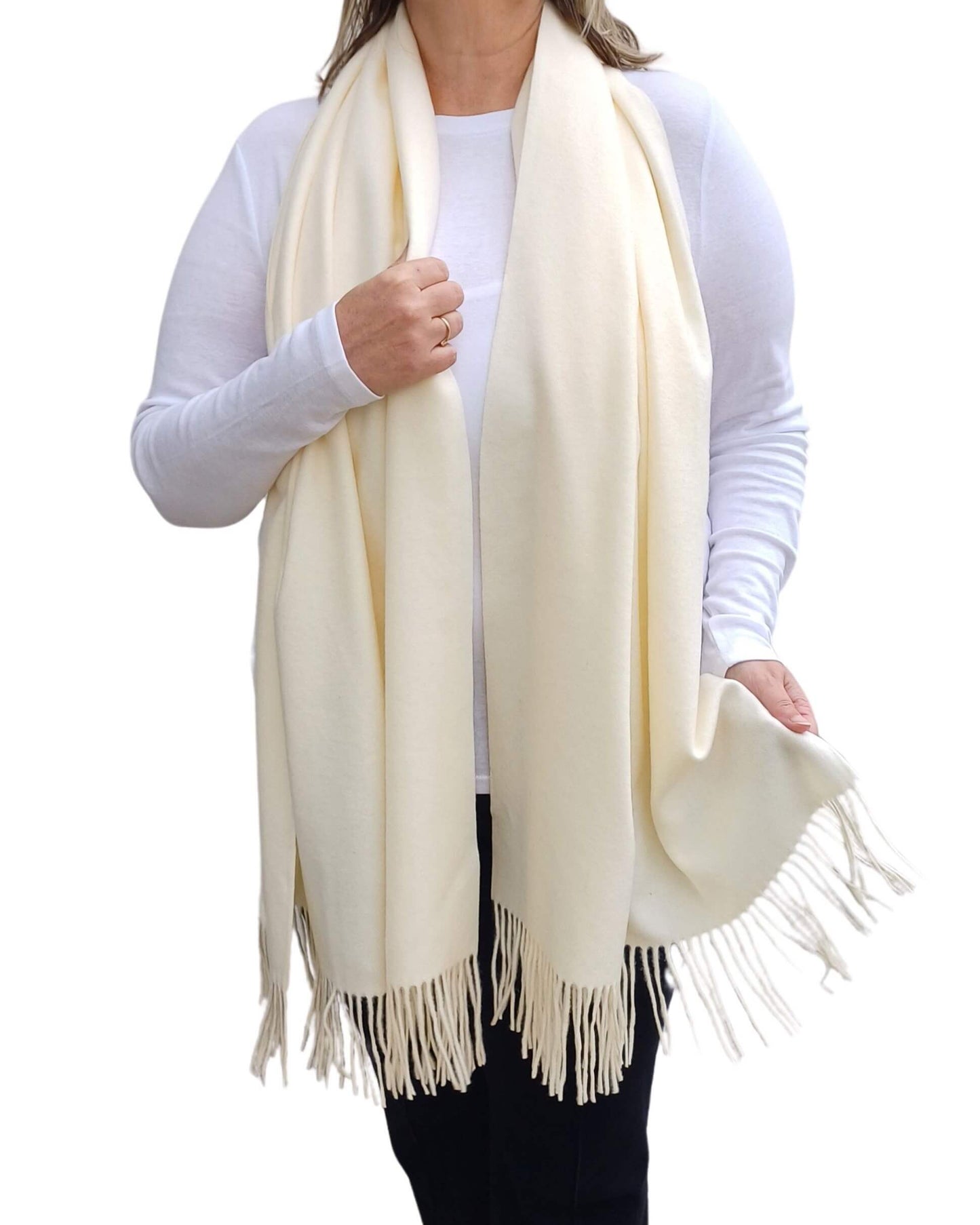 Aurora's Array: Woman models a soft, warm off-white cream wool blend scarf with fringed edges, draped around her neck and shoulders.