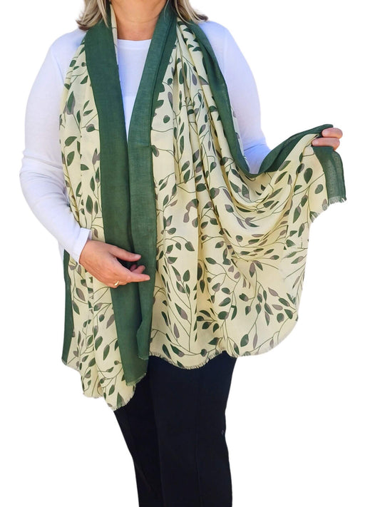 Aurora's Array: Woman models a soft, lightweight oversized scarf with a cream background, a green leafy print, and solid green borders.