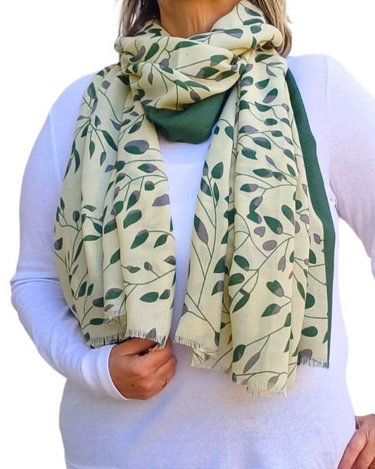 Aurora's Array: Woman models a soft, lightweight scarf with a cream background, a green leafy print, and solid green borders, wrapped around her neck.
