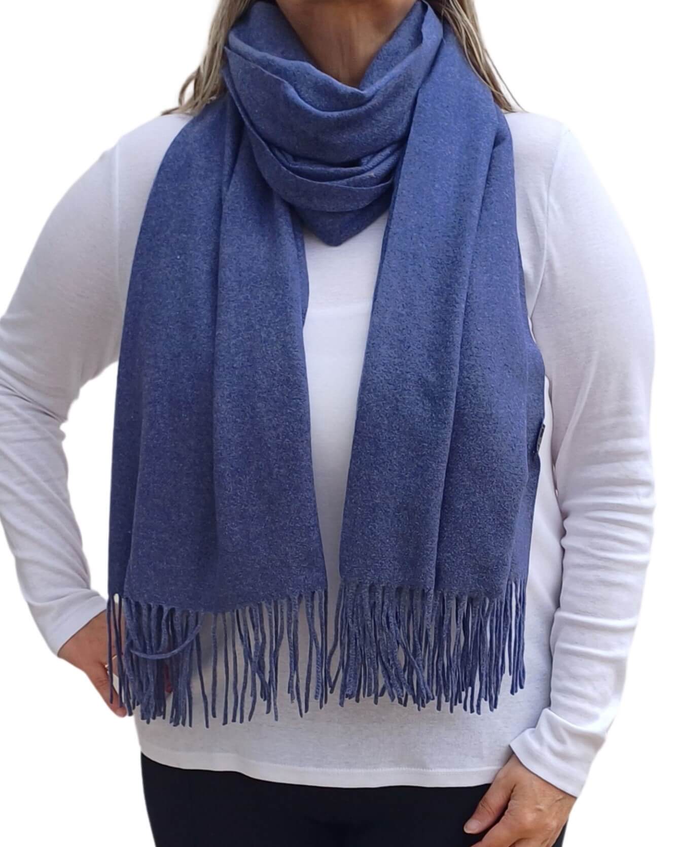 Aurora's Array: Woman models a soft, warm denim blue wool blend scarf with fringed edges, draped around her neck and shoulders.