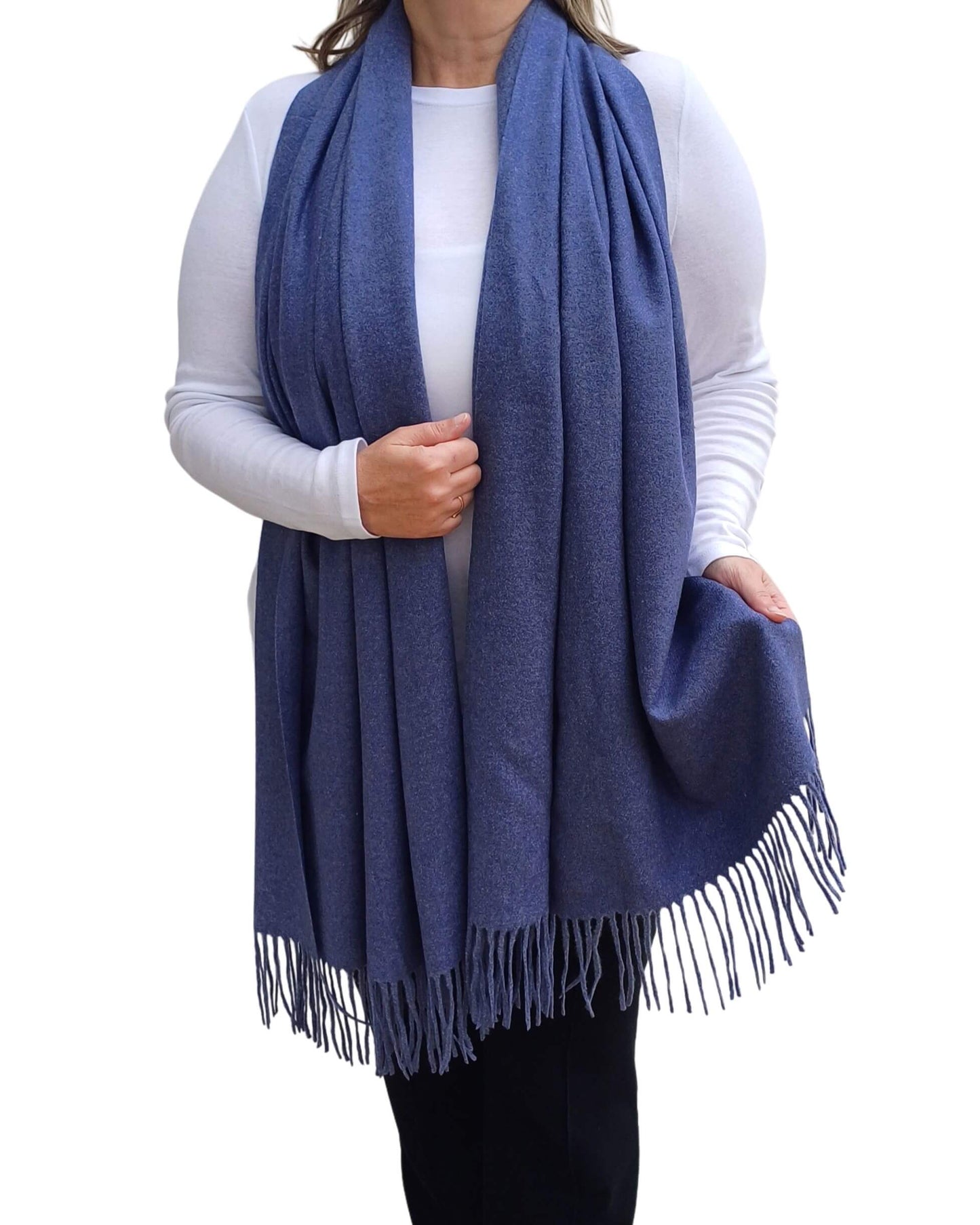 Aurora's Array: Woman models a soft, warm denim blue wool blend scarf with fringed edges, draped around her neck and shoulders.