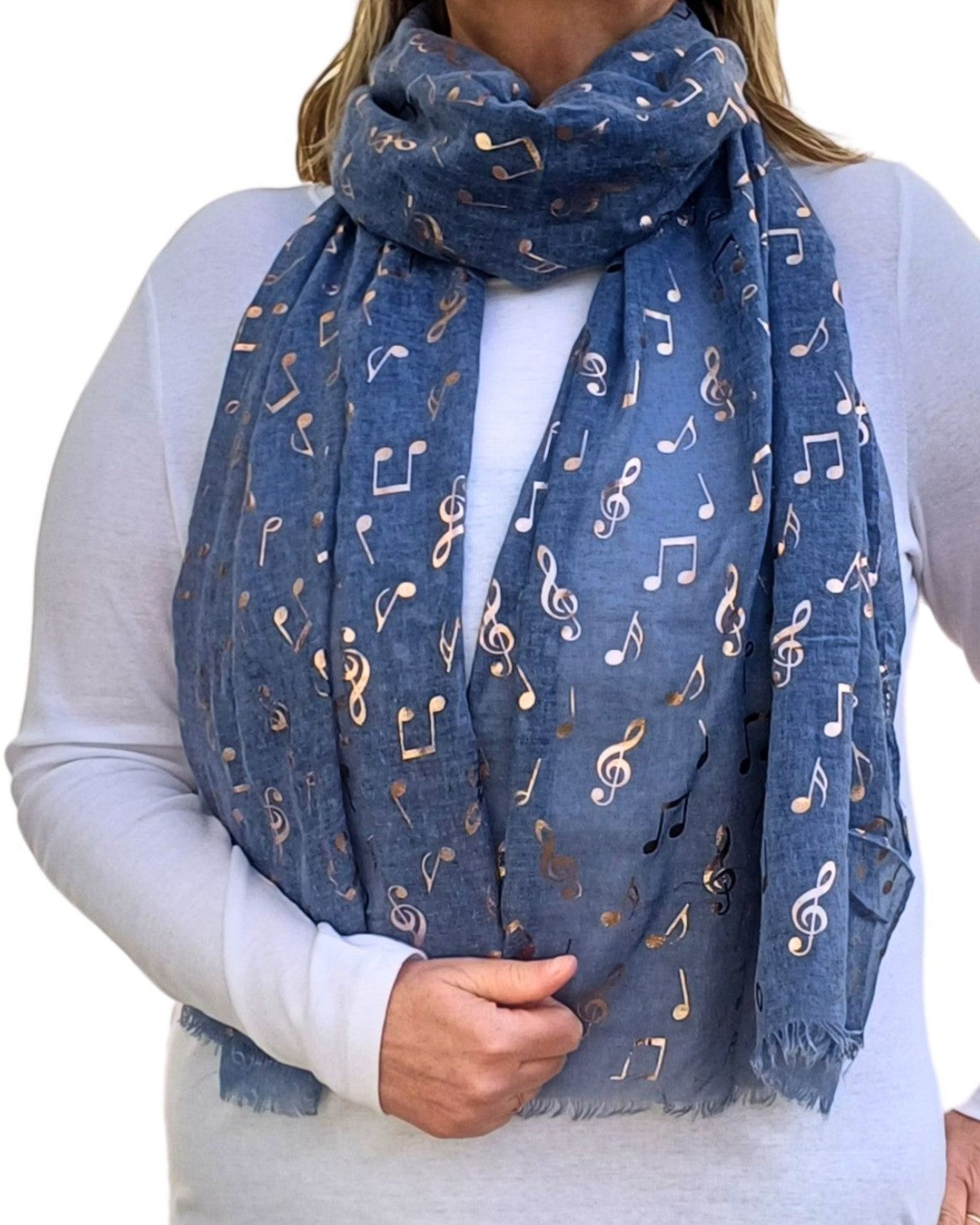 Aurora's Array: Muted denim blue scarf featuring a rose gold pattern of musical symbols, draped around a person wearing a white long-sleeved shirt.