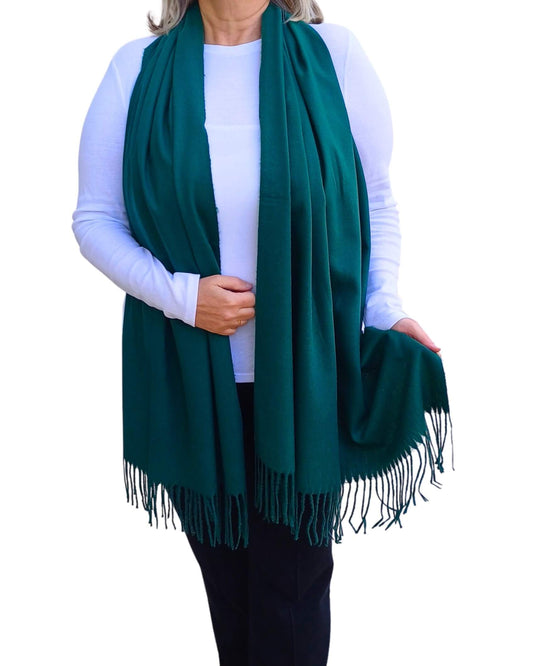 Aurora's Array: Woman models a soft, warm forest green wool blend scarf with fringed edges, draped around her neck and shoulders.