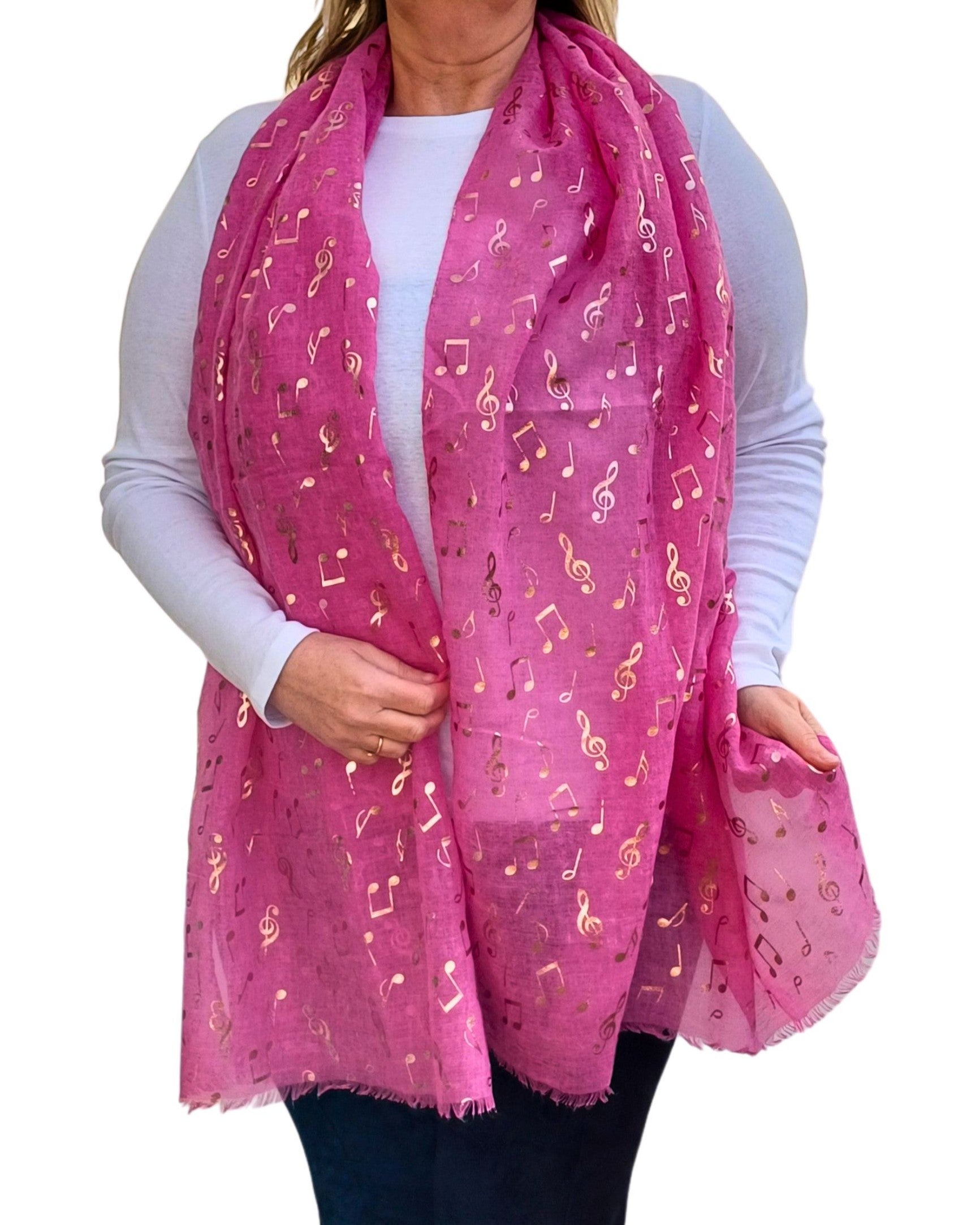 Aurora's Array: A woman wearing a long fuchsia pink scarf adorned with shiny rose gold music note prints. The scarf is styled loosely around her neck and drapes over a plain white long-sleeve top, paired with dark trousers.