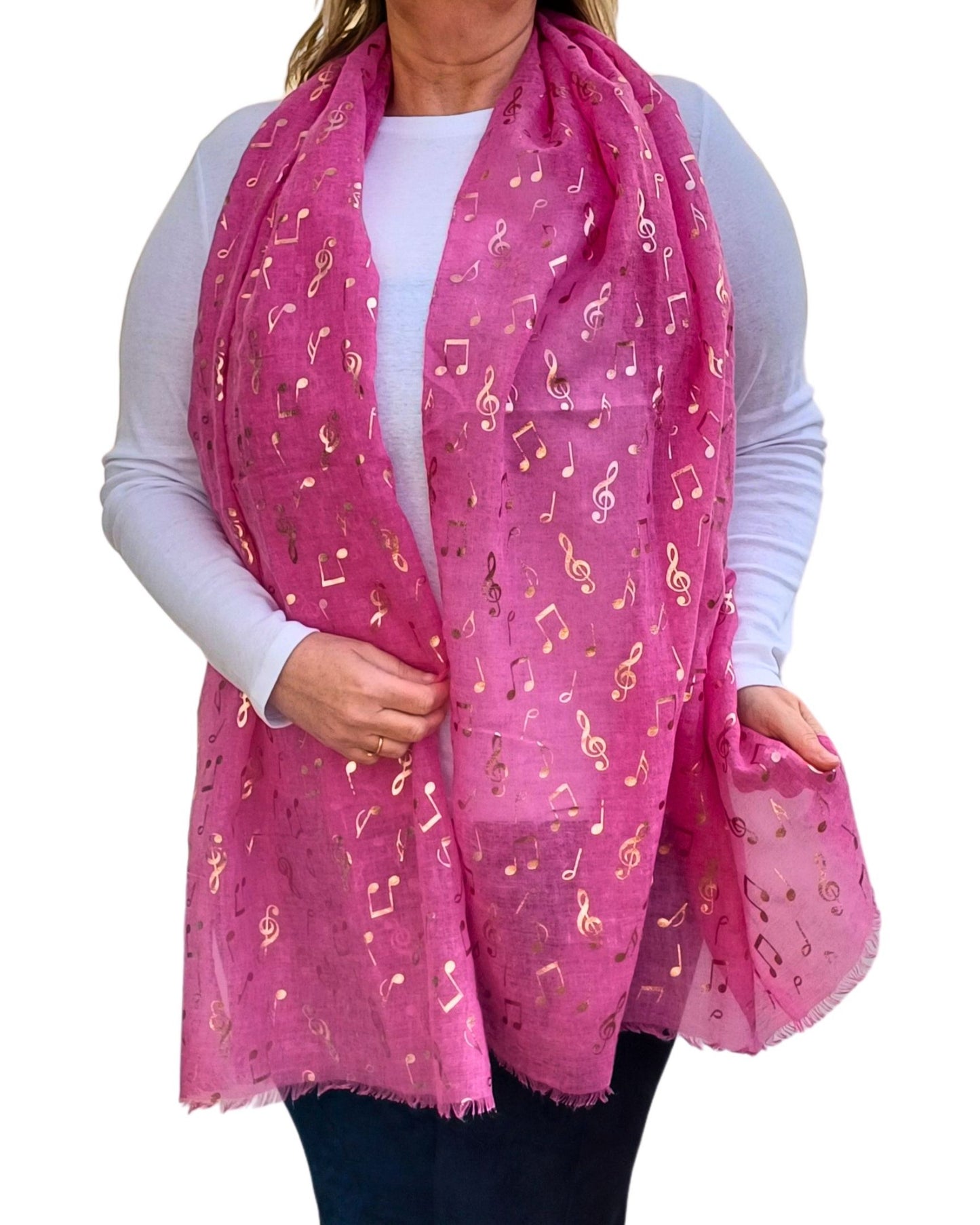 Aurora's Array: A woman wearing a long fuchsia pink scarf adorned with shiny rose gold music note prints. The scarf is styled loosely around her neck and drapes over a plain white long-sleeve top, paired with dark trousers.