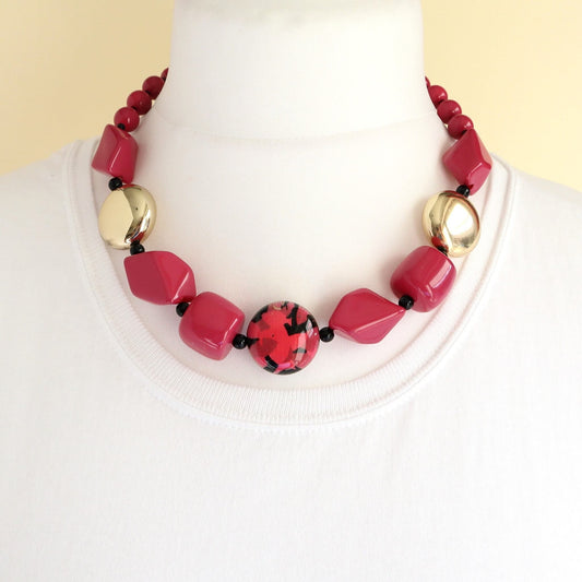 Short statement necklace with fuchsia pink faceted beads, shiny gold spheres, and a central red and black patterned round bead.