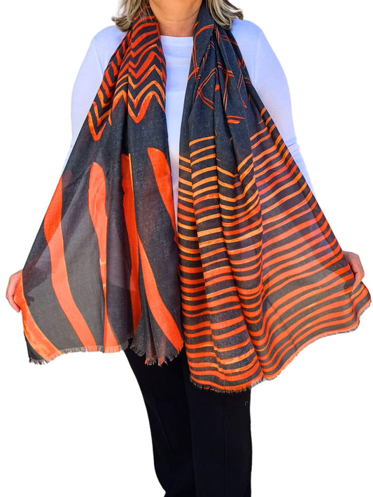 Aurora's Array: Woman models a soft, lightweight oversized scarf with a grey and orange geometric print and frayed edges.
