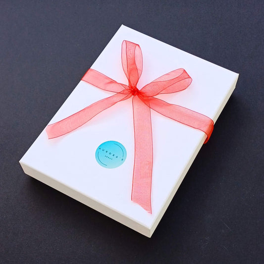 White rectangular gift box tied with a sheer red ribbon in a bow. A round blue sticker with "AURORA'S ARRAY" is on the box.