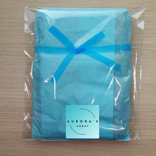 Item wrapped in light blue tissue paper, secured with a sheer blue ribbon and a teal "AURORA'S ARRAY" sticker. Enclosed in a clear cellophane bag.