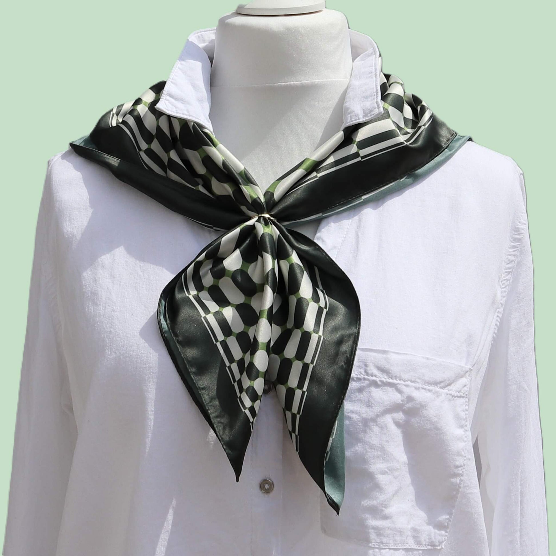 Aurora's Array: The Chic Satin Square Scarf - A dark green, light green, and white patterned satin scarf tied neatly around the neck of a mannequin wearing a white collared shirt.
