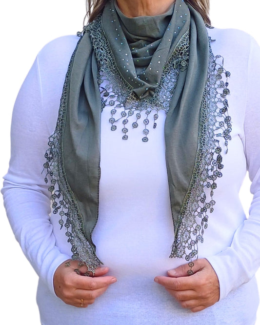 Aurora's Array: Woman models a soft, sage green lightweight scarf with delicate lace trim and subtle silver embellishments.