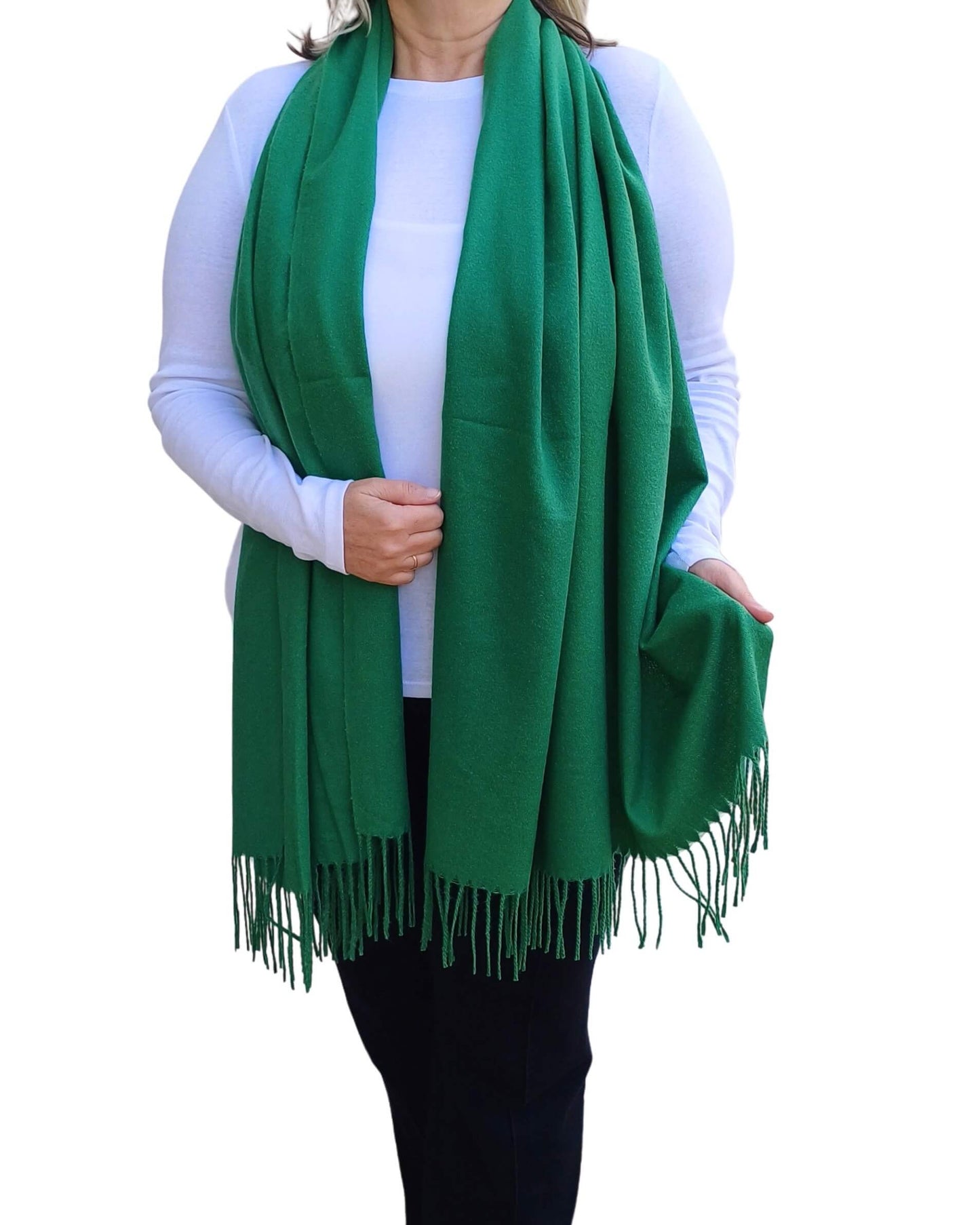 Aurora's Array: Woman models a soft, warm emerald green wool blend scarf with fringed edges, draped around her neck and shoulders.