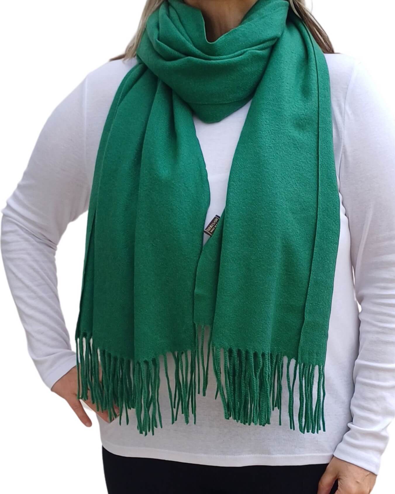 Aurora's Array: Woman models a soft, warm emerald green wool blend scarf with fringed edges, draped around her neck and shoulders.