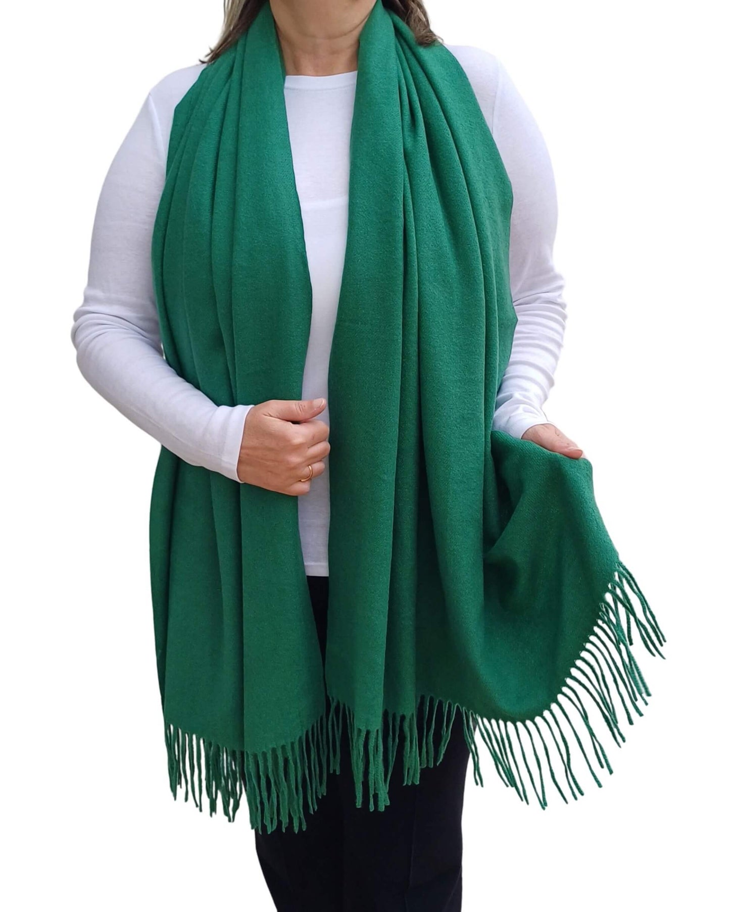 Aurora's Array: Woman models a soft, warm emerald green wool blend scarf with fringed edges, draped around her neck and shoulders.