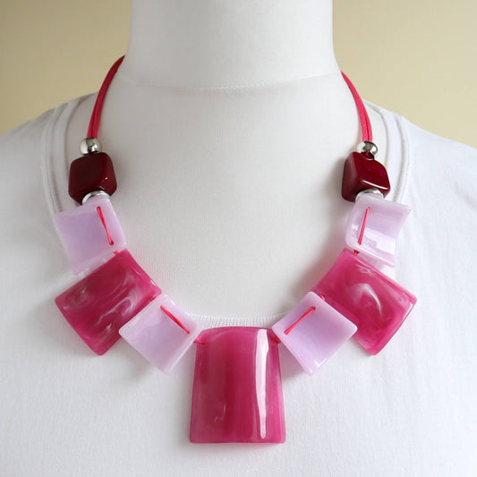 Bold statement necklace with glossy pink, light pink marble, and dark red square and rectangular beads. Strung on a bright pink cord with silver details.