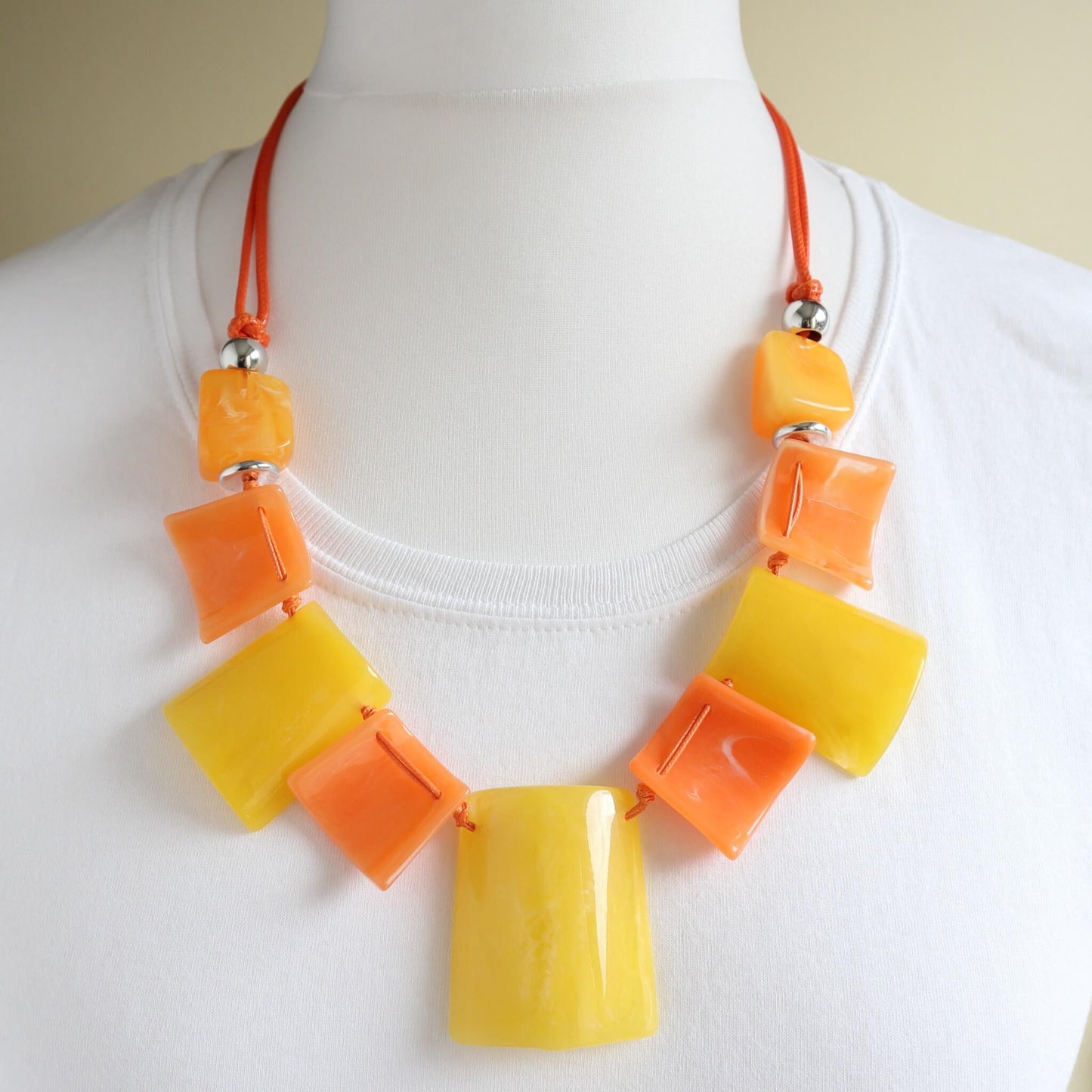 Vibrant statement necklace with glossy yellow and orange square and rectangular beads. Strung on a bright orange cord with silver-tone details.
