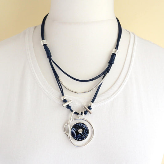Modern layered statement necklace with navy blue cords and silver-toned accents. Features a circular pendant with a blue and white marbled centre.