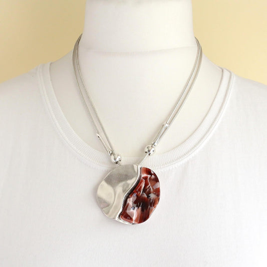 Silver tone multi-strand necklace featuring a wavy, split pendant with a red marble-effect inlay on one side. Adjustable length.
