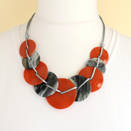 Lightweight statement necklace with alternating orange and grey marbled flat round beads. Connected by silver-toned wire. Modern design.