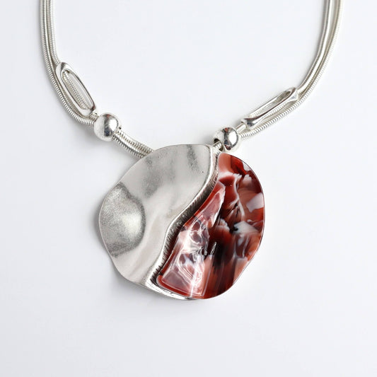 Silver tone necklace with a wavy, abstract pendant. One half is textured silver, the other features a red and white marbled effect.